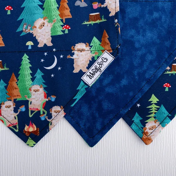 Close up of dog bandana with Sasquatch and forest theme, navy background.