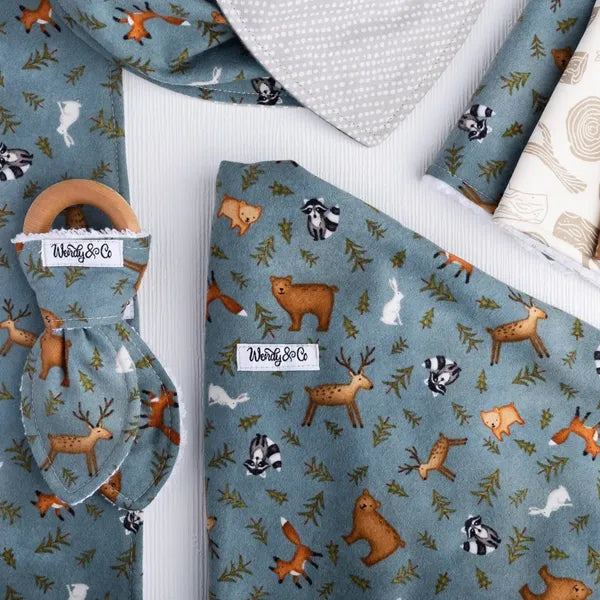 Whispering Woods baby collection with bib, blanket, burp cloth, teether, washcloth, and hairbow in forest print.