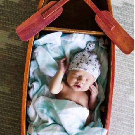 Newborn baby in row boat with soft beanie.