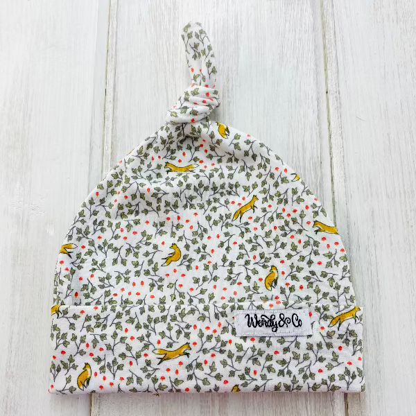 Soft stretchy knit beanie with ivy vines and red flowers and little orange foxes playing in the leaves.