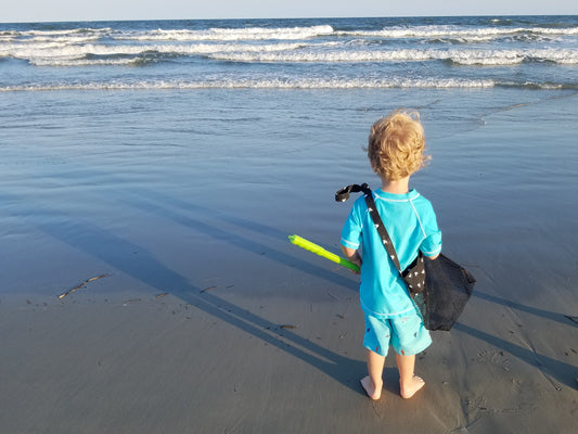 Little boy looking at ocean with seashell bag and shovel.
