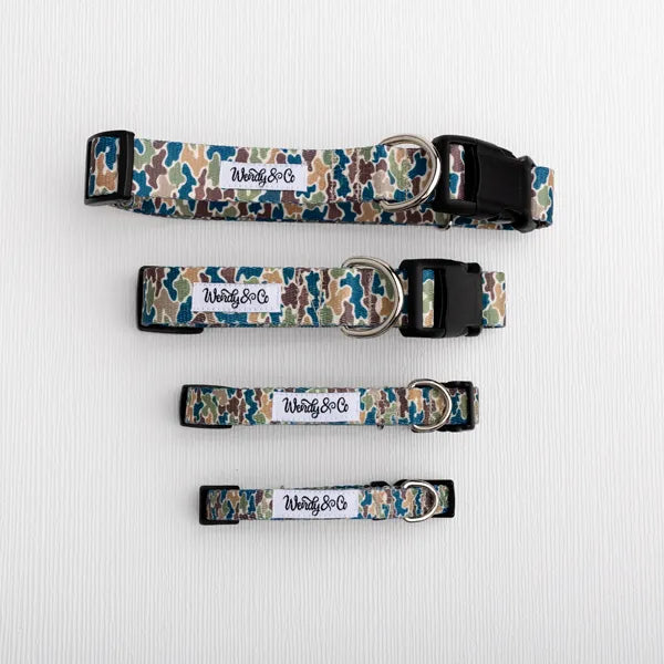Four dog collars with a blue, green, and beige camouflage pattern, laid out vertically on a white textured background. Each collar has a white rectangular label with the brand name 'Wendy&Co' and a black plastic buckle.