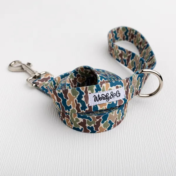 A dog leash with a blue, green, and brown camouflage pattern, featuring a silver metal clasp and a D-ring, with a white brand label reading 'Wendy & Co'.