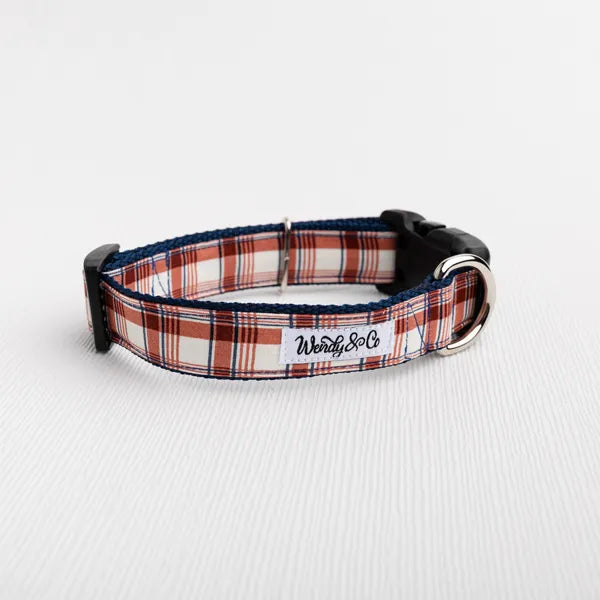 A dog collar with a red, white, and navy plaid pattern, featuring a black plastic buckle, silver metal hardware.