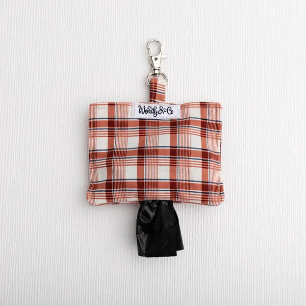 A small plaid dog poop bag holder pouch with a silver clasp and a black bag pulled out, shown on a white textured background.