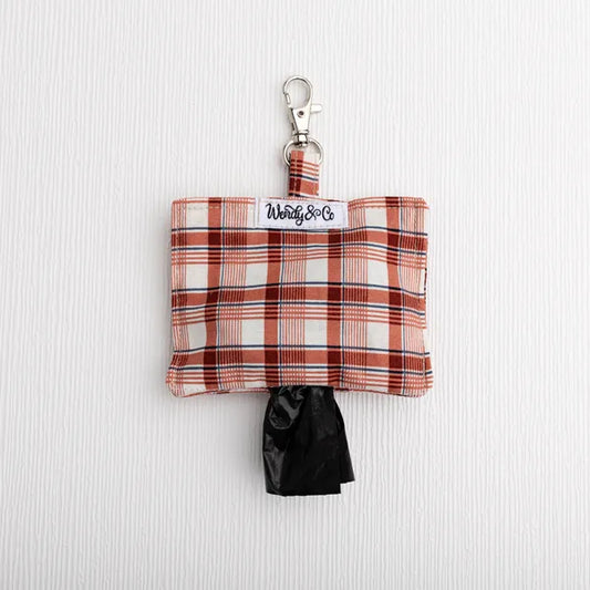 A small plaid dog poop bag holder pouch with a silver clasp and a black bag pulled out, shown on a white textured background.