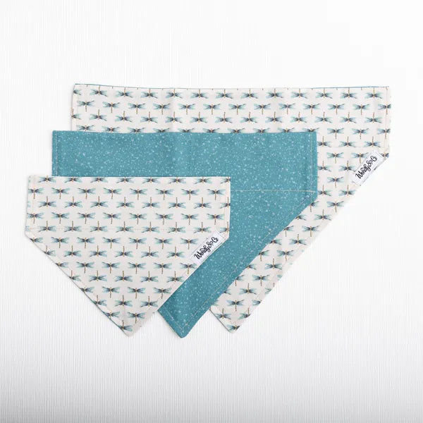 Three triangular bandana-style pet collars or bibs overlapping on a white background. Two have a white base with a repeating blue and gray dragonfly pattern, and one has a solid teal-blue fabric backing.