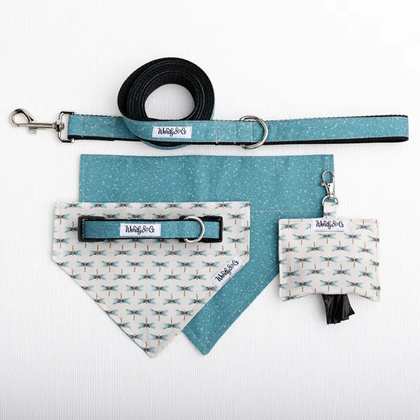 A pet accessory set laid flat on a white textured background, including a teal and white patterned bandana with dragonfly, matching leash, pouch, and a black leash strap with metal hardware. 