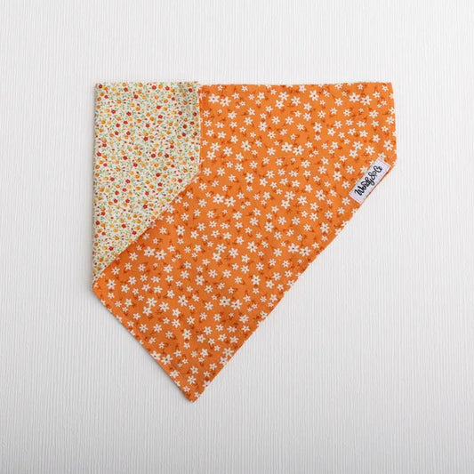 A triangular pet bandana with a two-sided floral print. One side features a vibrant orange background with small white daisy-like flowers, while the reverse side shows a cream background with orange and red floral motifs.