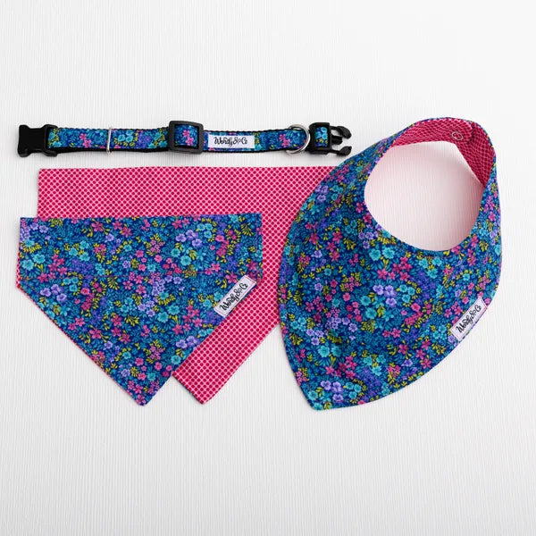 A pet accessory set including a bandana collar, a triangular bandana, and a bib, all in matching blue floral fabric with pink gingham backing, displayed on a white background.