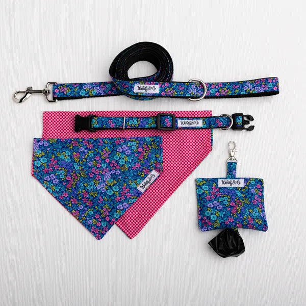 A pet accessory set laid out on a white background, including a floral-patterned leash, matching collar, bandana, pouch, and black glove bag. The set features blue, purple, and pink floral fabrics with some pink gingham sections, and each item has a small white label reading Wendy&Co.