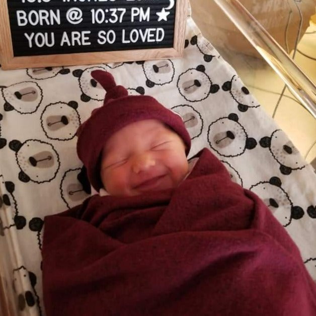Newborn baby swaddled and wearing a top knot beanie.