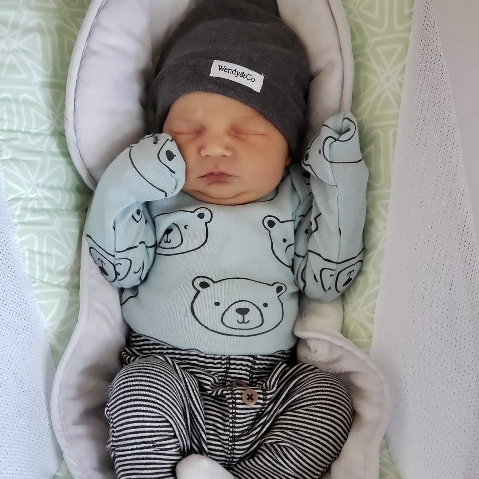 Newborn baby sleeping with bear print clothing and soft beanie with top knot.