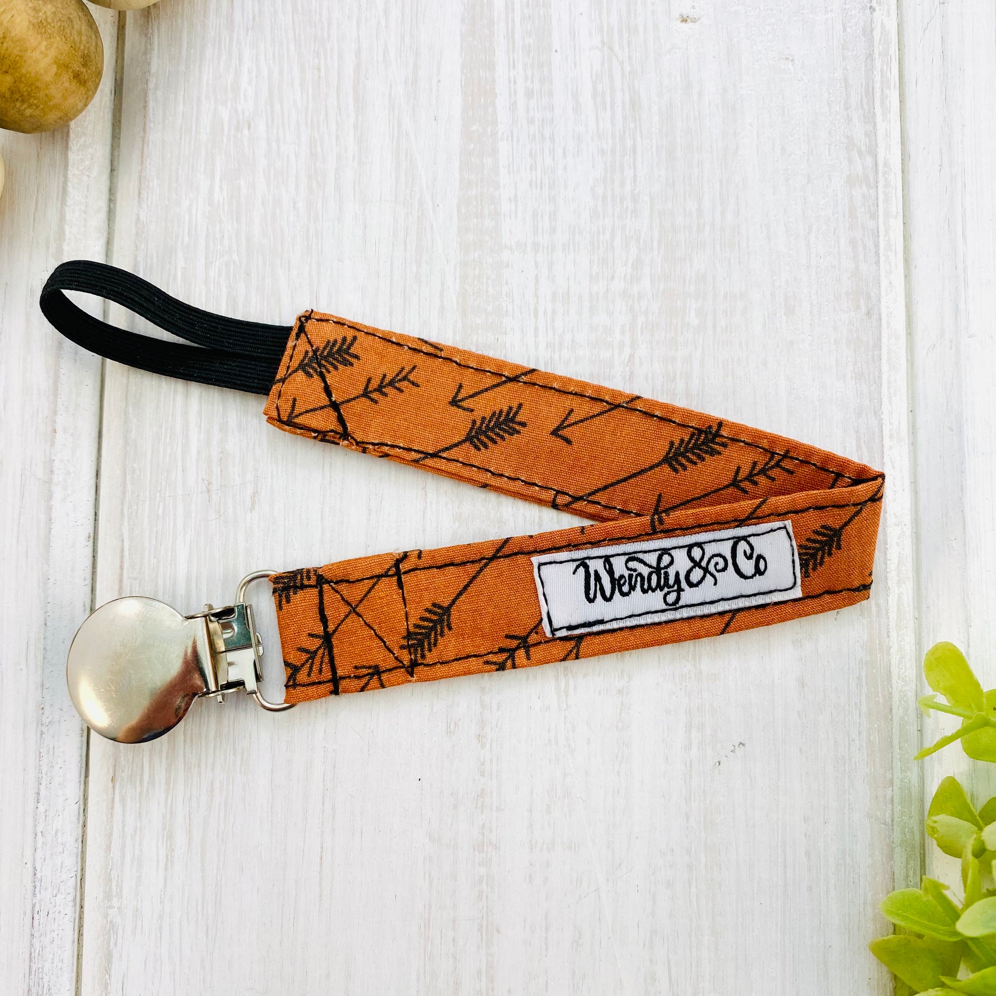 Pacifier clip or soother holder for baby in Boho rust with black arrows.