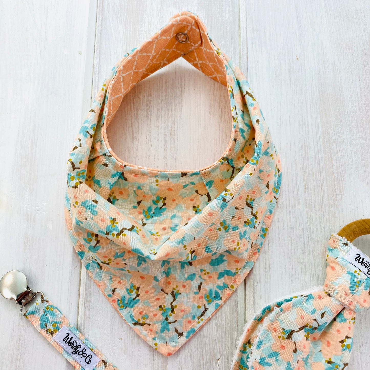 Handcrafted baby bib in peach and mint floral dogwood pattern.