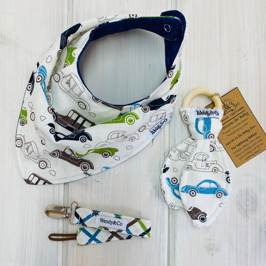 Linen cream bandana baby bib with model T cars in brown, green and blue, reversible to navy. Shown with coordinating teether and paci clip.