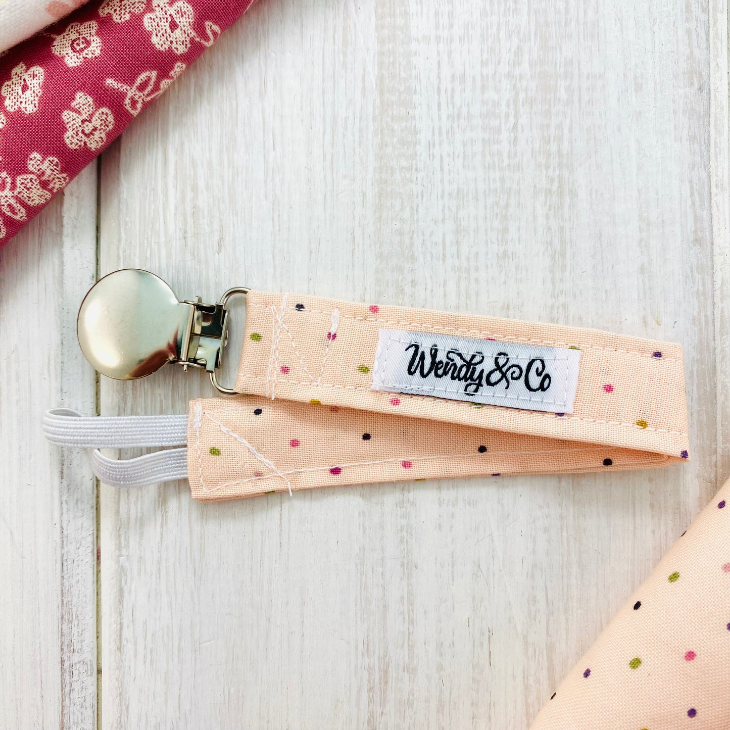 Girly blush pacifier clip with dainty polka dots.