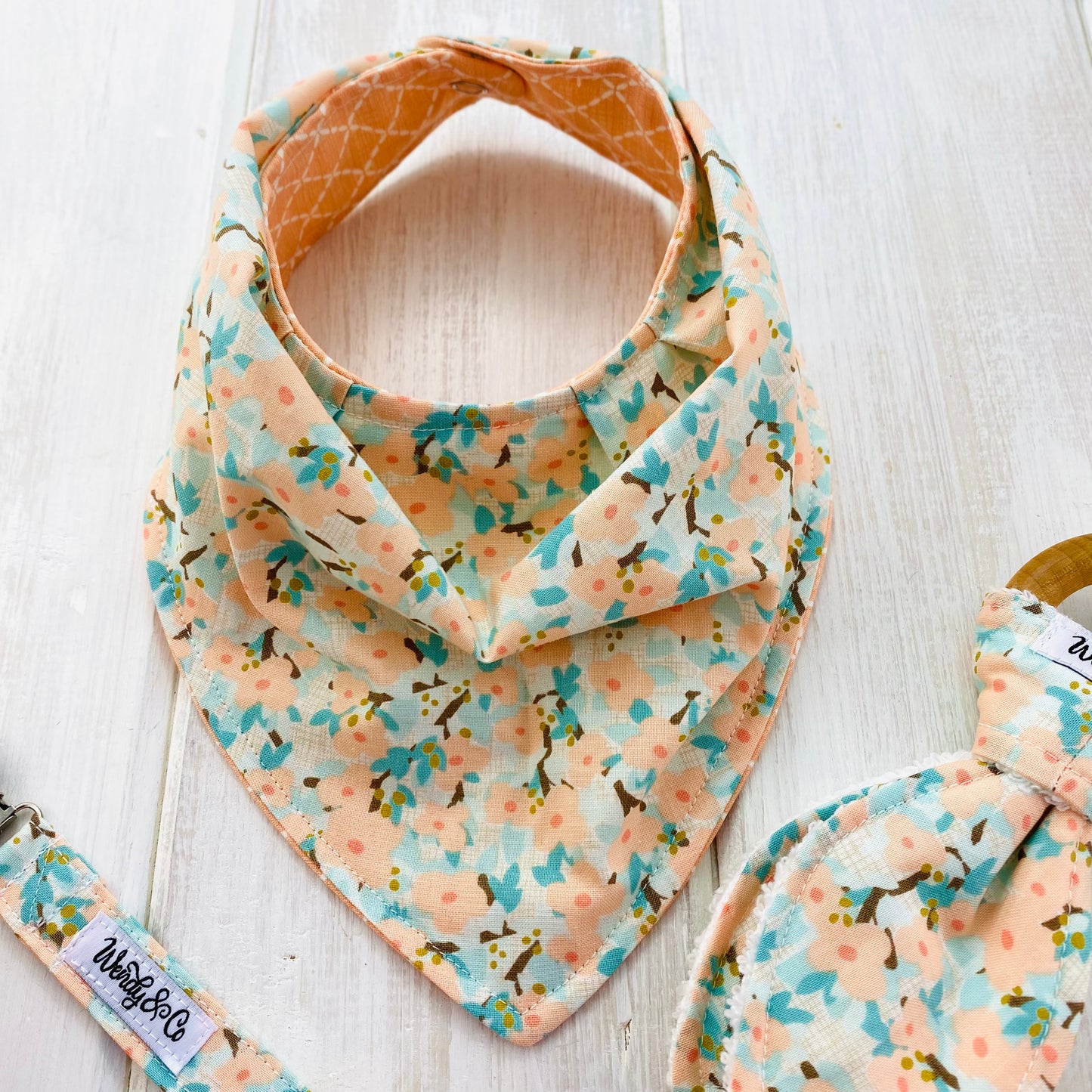 Baby bandana bib in peach lattice on one side and peach dogwood flowers on the other side.