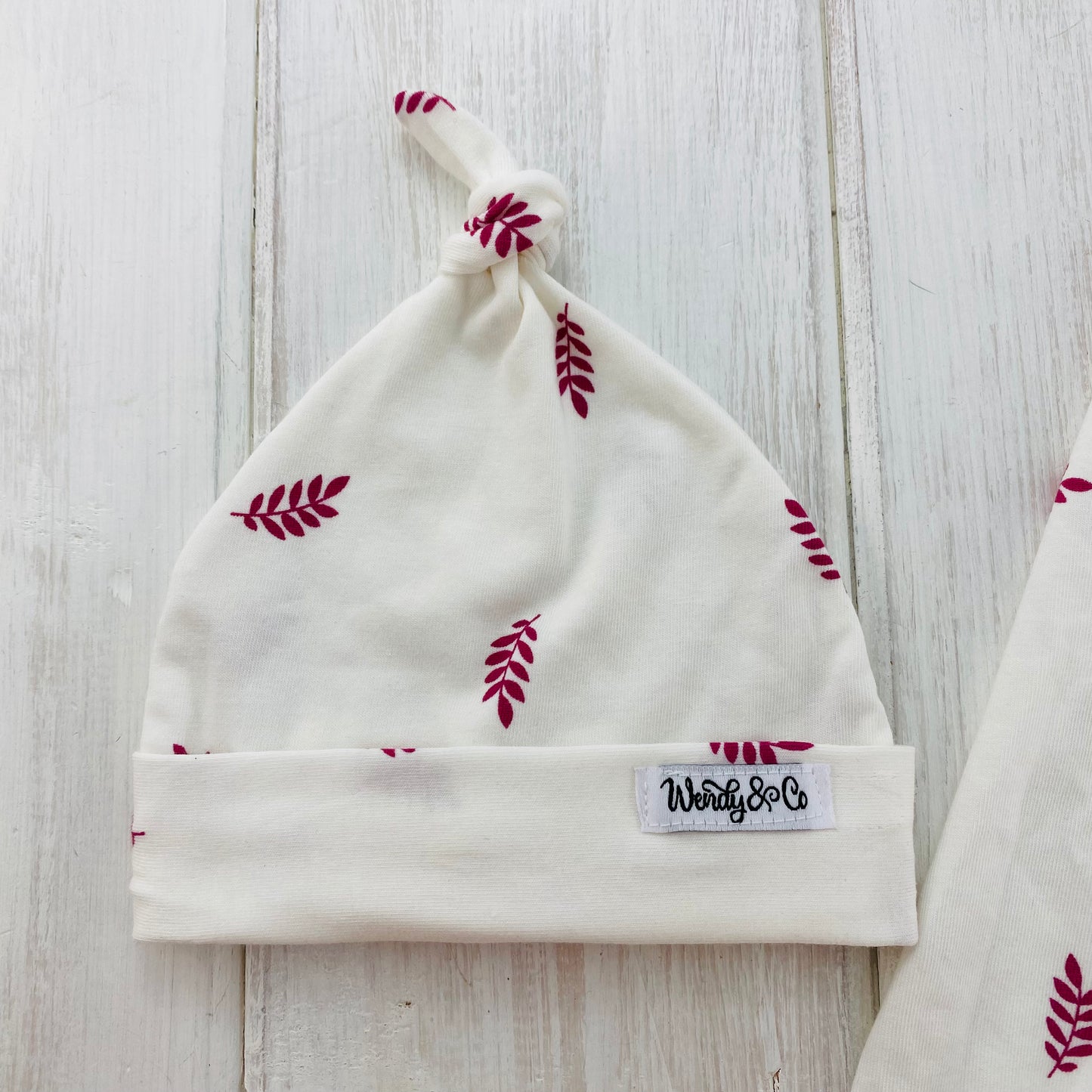 Delicate white with scattered raspberry leaves on newborn hat.